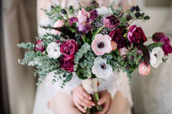 A bouquet of mixed flowers with shades of pink, white, and deep red, held by a person.