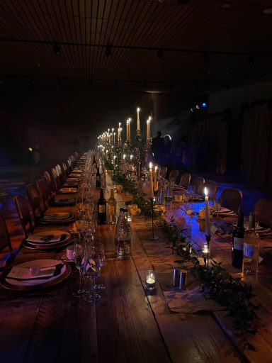 Elegant long table set for dinner, adorned with candles and floral arrangements.