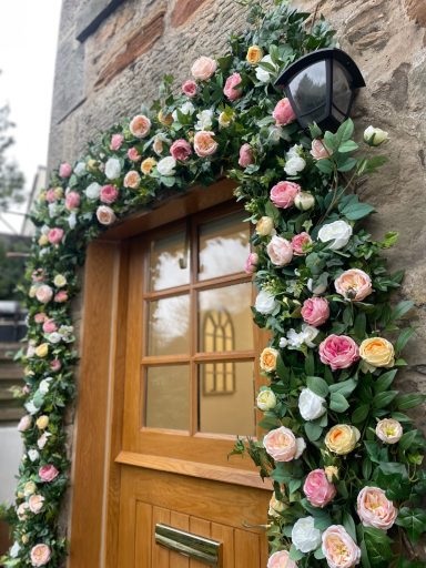 Doorway adorned with a floral arch of pastel roses and greenery.
