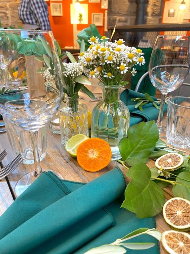 Table setting with flowers, fruit, and green cloth, creating an inviting dining atmosphere.