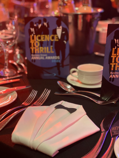 Table set for an event, featuring a menu titled "Licence to Thrill" and elegant tableware.