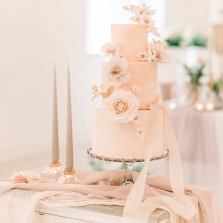 Chiffon Cake Table Decor Package Three-tiered pastel pink wedding cake adorned with floral decorations and elegant candles.