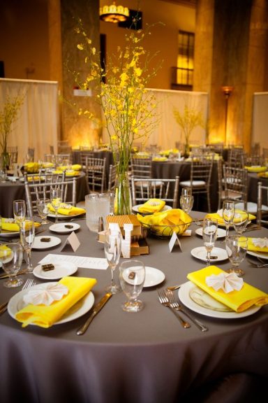 Elegant dining setup with grey tablecloth, yellow napkins, and floral centrepieces.