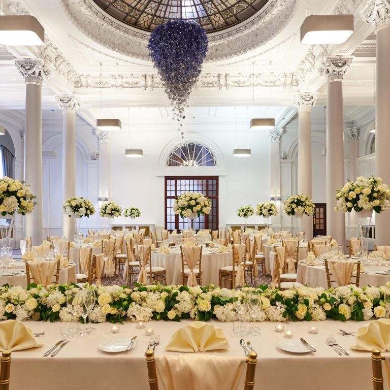 George Hotel Cream Linens Elegant banquet hall set for a wedding with floral arrangements and golden decor.