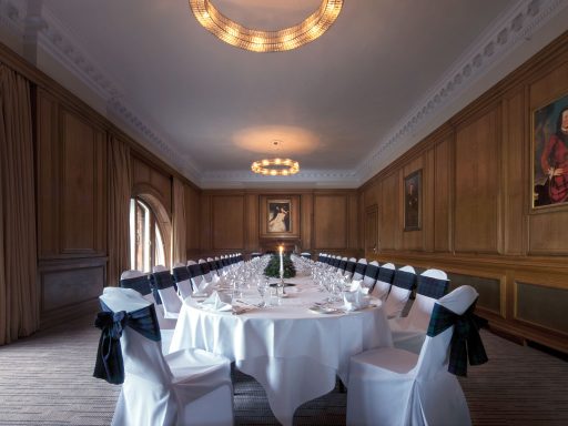 Elegant dining room with a round table, white tablecloth, and chairs adorned with black sashes.