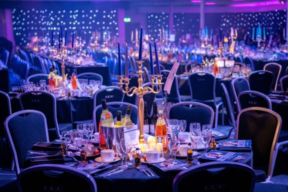 Elegant banquet setup with tables, candles, and a vibrant purple-lit background.
