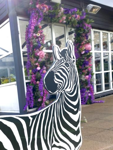 A zebra cutout in front of a building adorned with purple flowers.