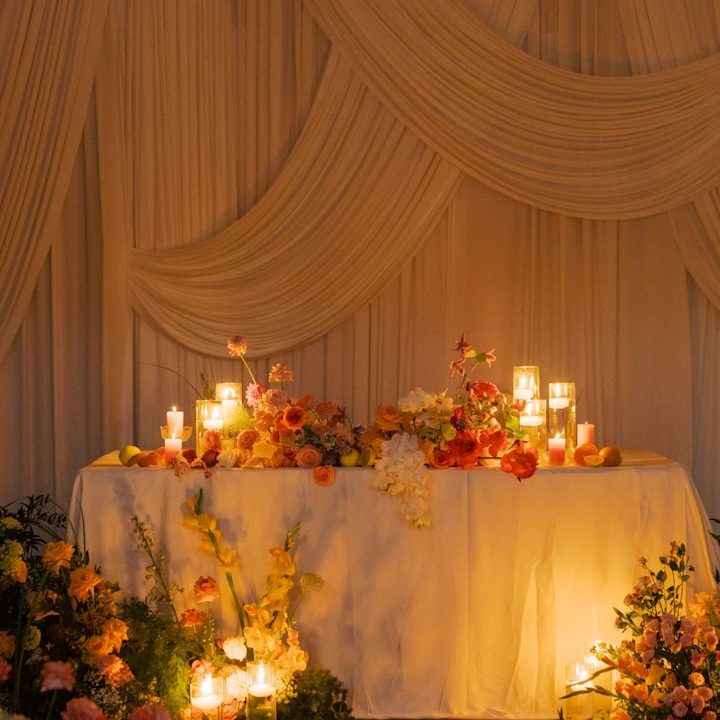 Wedding Draping, Florals and Candles A decorated table with flowers and lit candles against a draped backdrop.