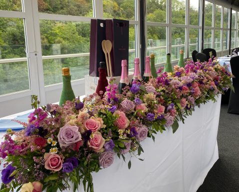 A floral arrangement with champagne bottles on a table, set against a scenic backdrop.