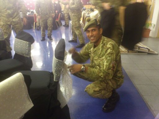 Soldier in military uniform smiling while adjusting chair covers at an event.