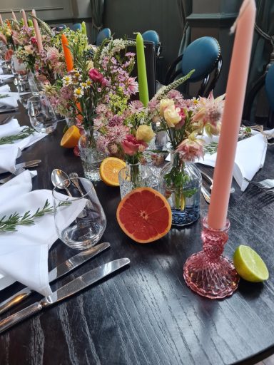 A beautifully set dining table with flowers, citrus fruits, and pink candles.